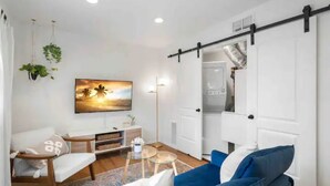 Un salon moderne avec un canapé bleu, une table basse et un tableau représentant un coucher de soleil.
