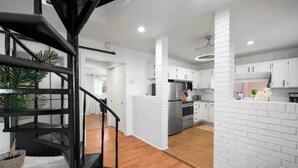Une cuisine moderne avec des meubles blancs, un îlot central et un escalier en colimaçon noir.