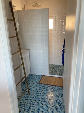 A bathroom with a shower, a toilet, and a small window.