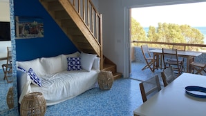Ein Zimmer mit blau-weißen Fliesen, einem weißen Sofa mit gemusterten Kissen, einer Holztreppe und einem Balkon mit Tisch und Stühlen.