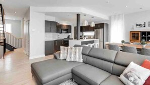 Una sala de estar moderna con un sofá seccional gris, una escalera y una cocina al fondo.