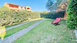 Un jardín con una silla de descanso roja, un camino de piedra y un edificio con paredes y arcos anaranjados.