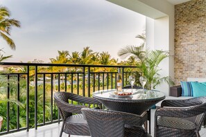 Enjoy al fresco dining on the balcony overlooking a serene garden with palm trees.