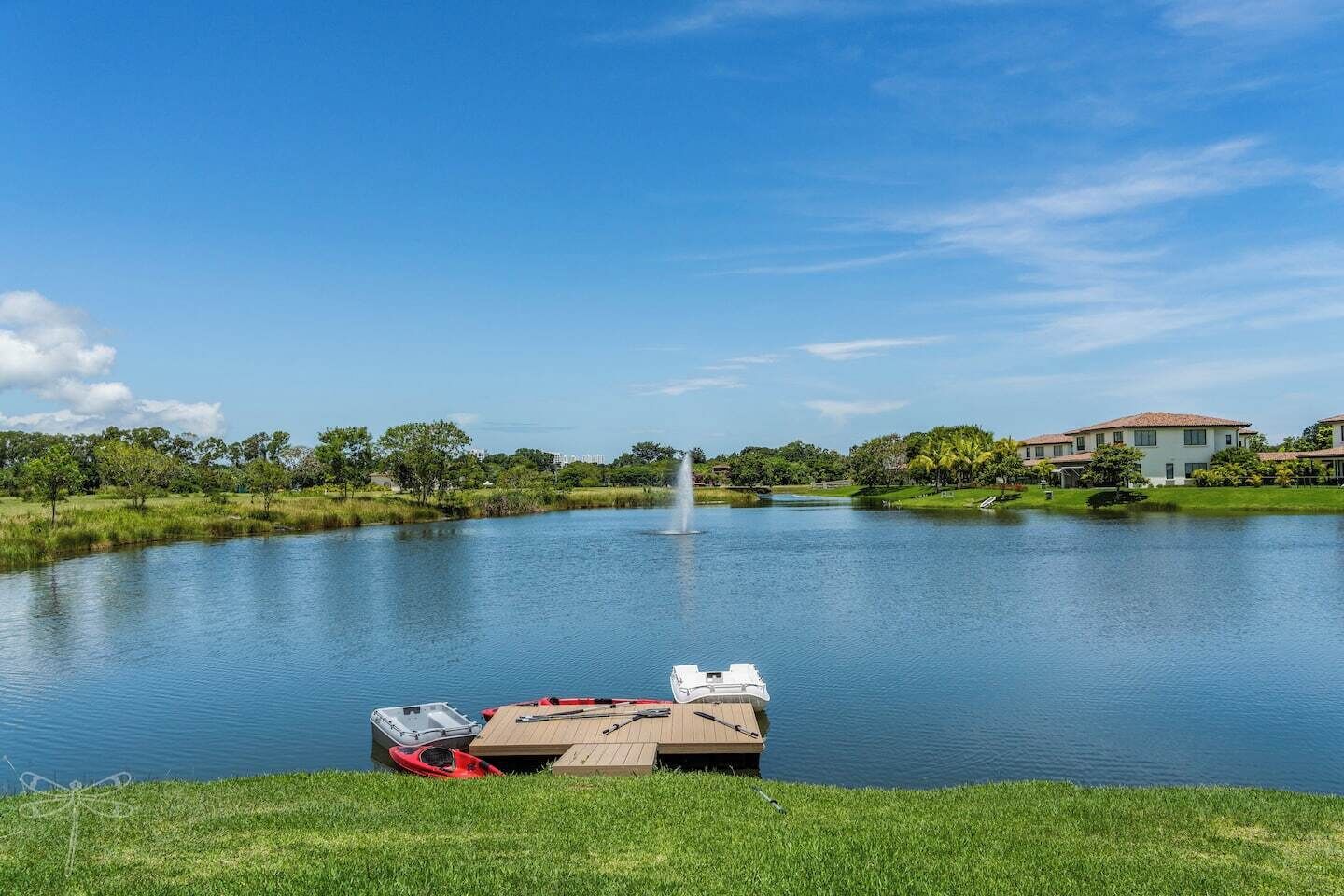 A tranquil lake with a dock, a fountain, and a building in the background.