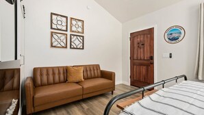 Ein Schlafzimmer mit einem braunen Ledersofa, einem Bett mit gestreifter Decke, einer Holztür und vier gerahmten Wandbildern.
