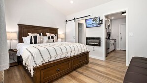Ein Schlafzimmer mit einem großen Bett, einem an der Wand befestigten Fernseher, Holzboden und einer Tür zu einem Badezimmer.