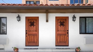 Ein Gebäude mit zwei symmetrischen Holztüren, jeweils mit einem kleinen Fenster darüber. An jeder Seite der Türen befinden sich zwei Wandleuchten.