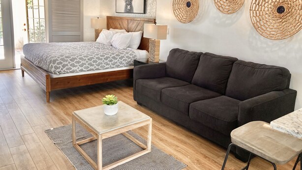 A modern bedroom with a bed, a dark sofa, a small table with a plant, and decorative woven wall art. - 34- Amira Resort Condo, Heated Pool, Hot tub, Gym (St. George)