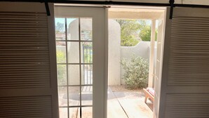A room with a bed, a window with shutters, and a view of a patio with a bench and greenery. - 34- Amira Resort Condo, Heated Pool, Hot tub, Gym (St. George)