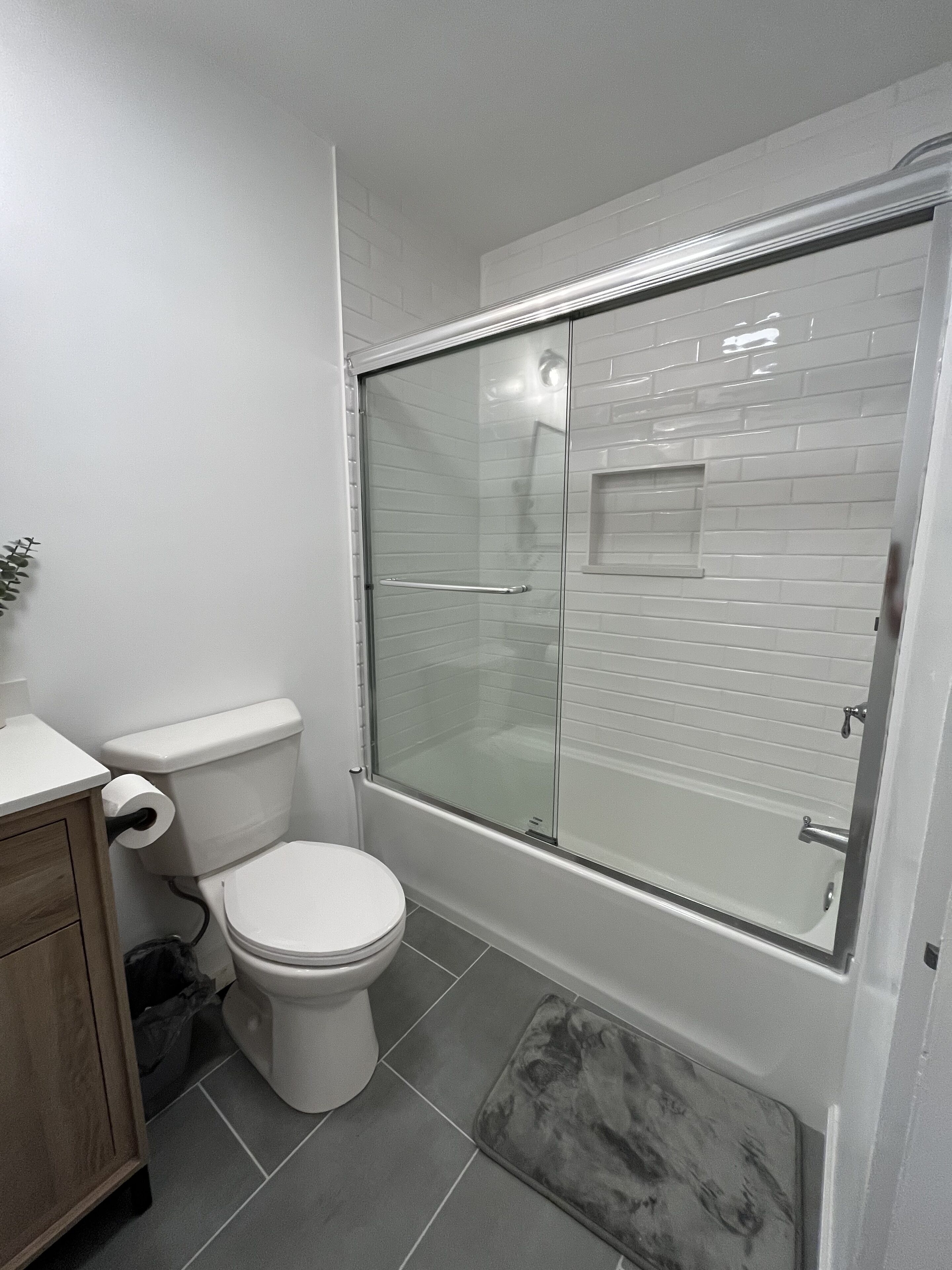 A bathroom with a toilet, a glass-enclosed shower, and a marble bath mat.