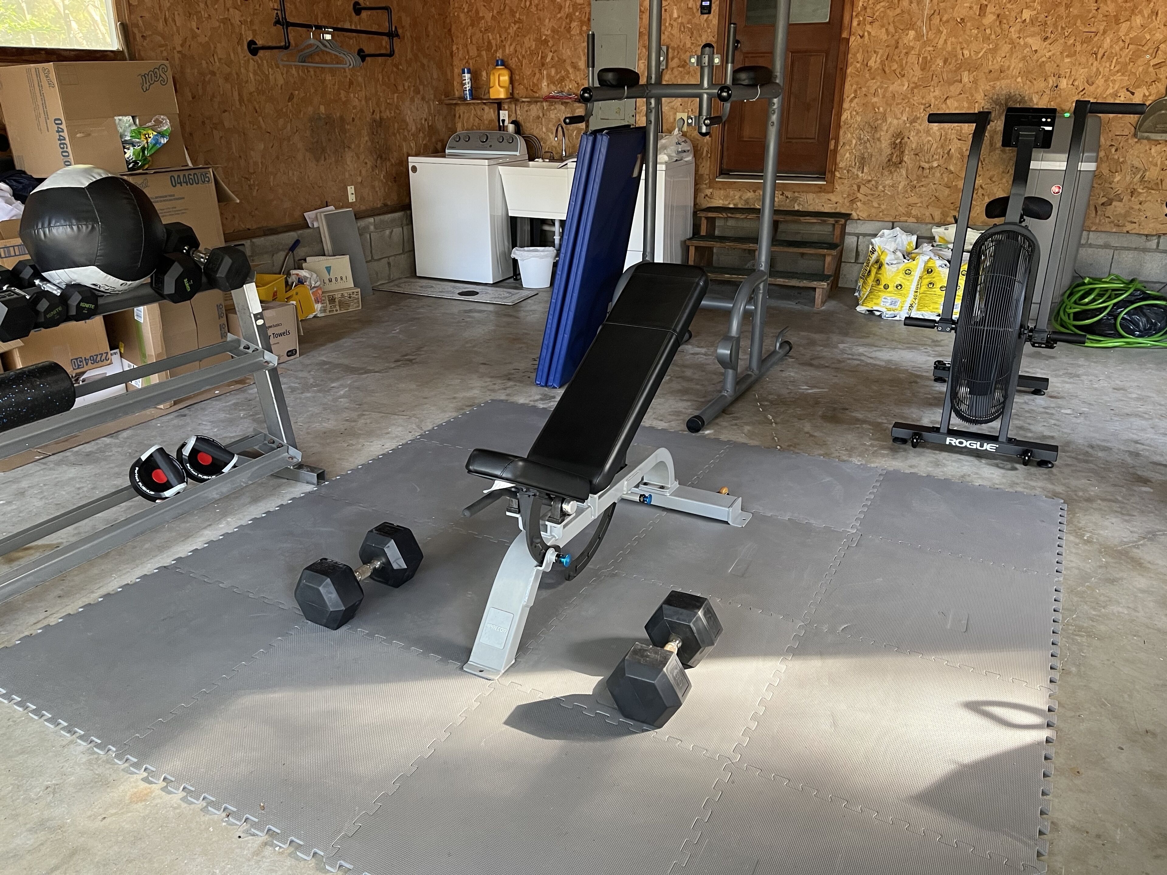 A home gym with a bench press, dumbbells, a treadmill, and a stationary bike.