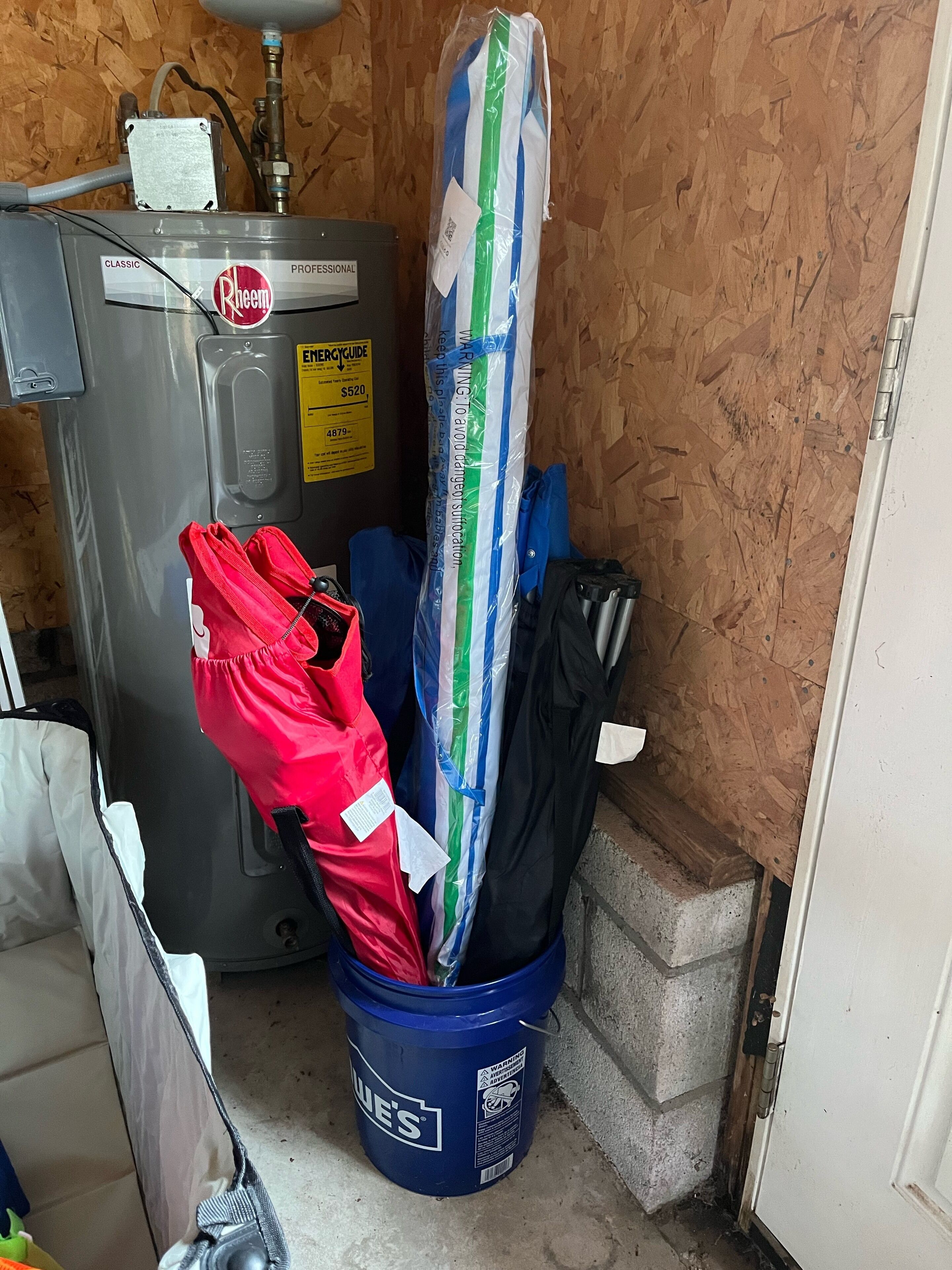 A utility room with a water heater, a bucket with a striped bag, and a red umbrella.