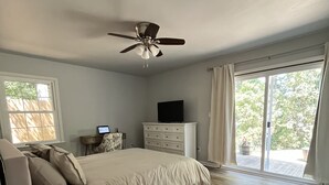 Une chambre à coucher avec un lit, un ventilateur de plafond, une commode, un téléviseur et une fenêtre avec des rideaux.