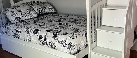 Un lit superposé avec un lit en bas et un lit en hauteur, tous deux dotés de linge de lit sur le thème de l’océan. Il y a trois tiroirs sur le côté du lit en hauteur.