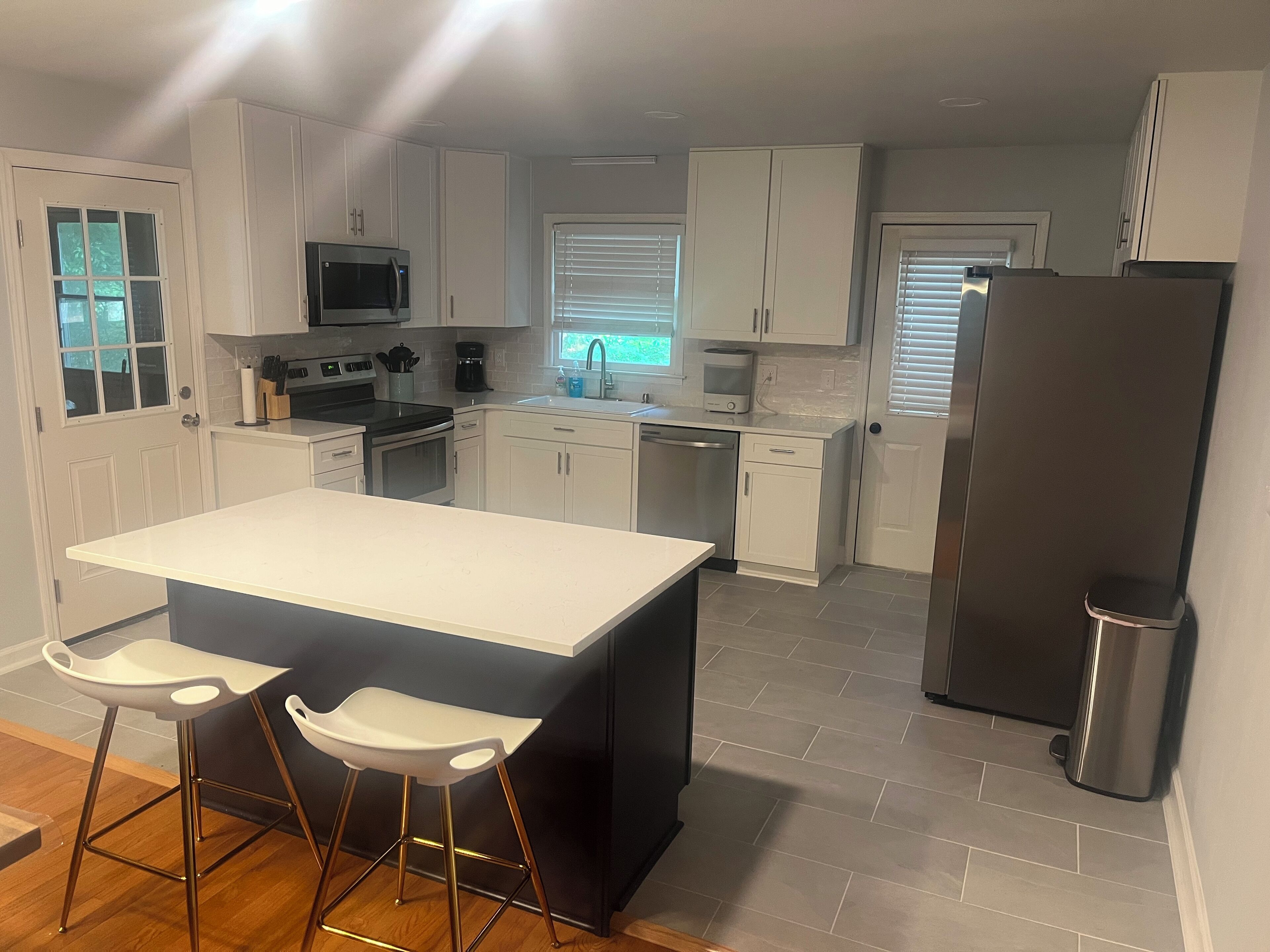 A modern kitchen with white cabinets, a stainless steel refrigerator, a central island with stools, and a dishwasher.