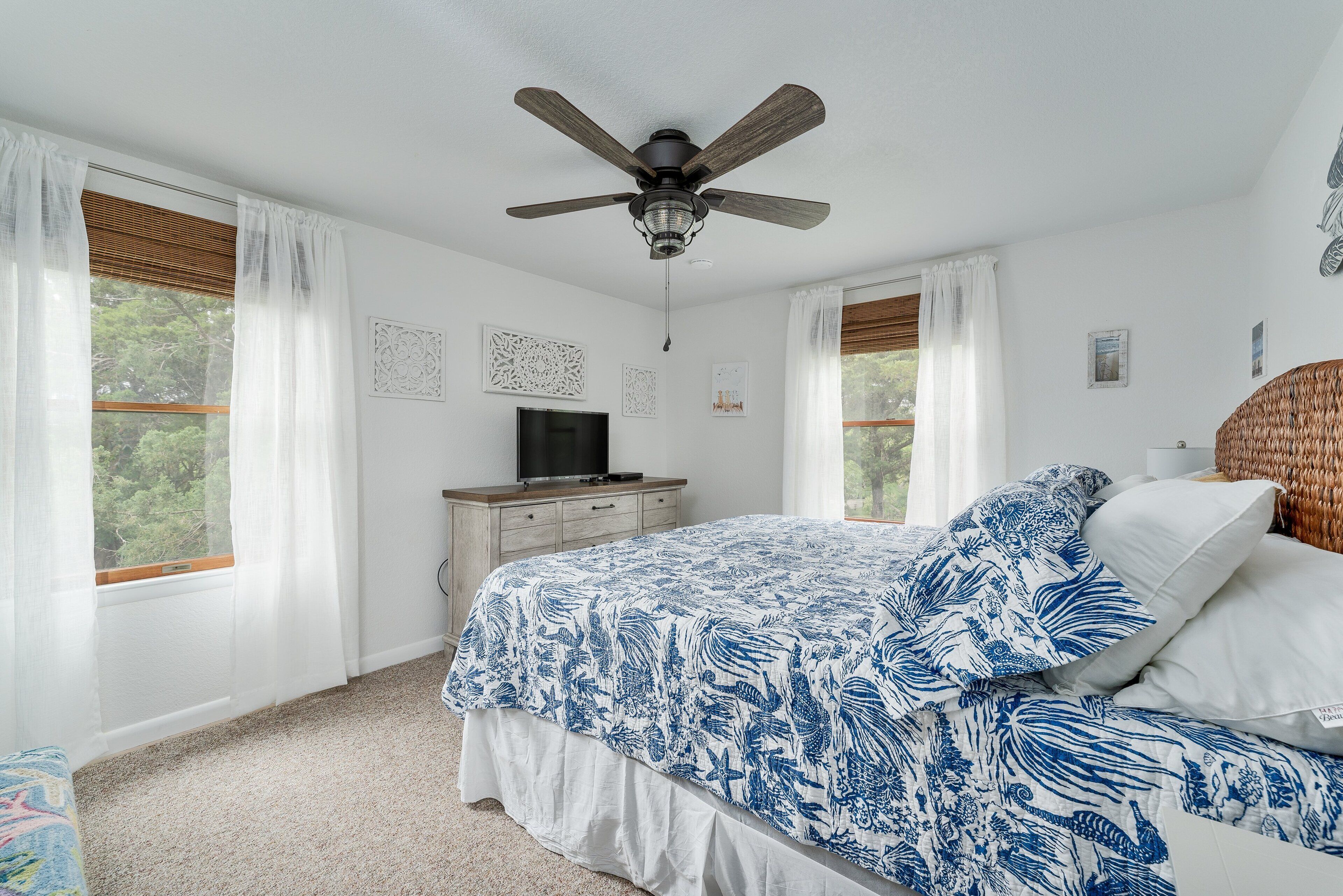 Une chambre à coucher comprenant un lit, un ventilateur de plafond, une commode, un téléviseur et des œuvres d’art accrochées aux murs.