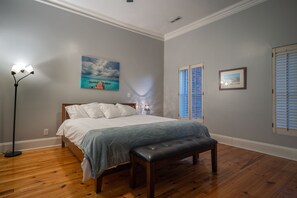 A bedroom with a bed, a bench, a floor lamp, and two windows with shutters.