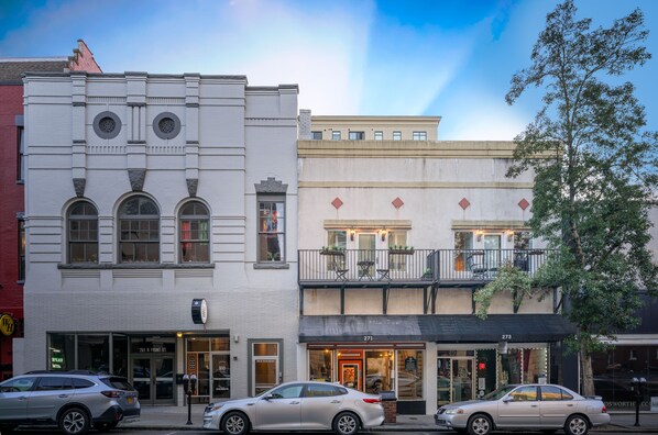 A street view with two-story buildings, storefronts, and parked cars.