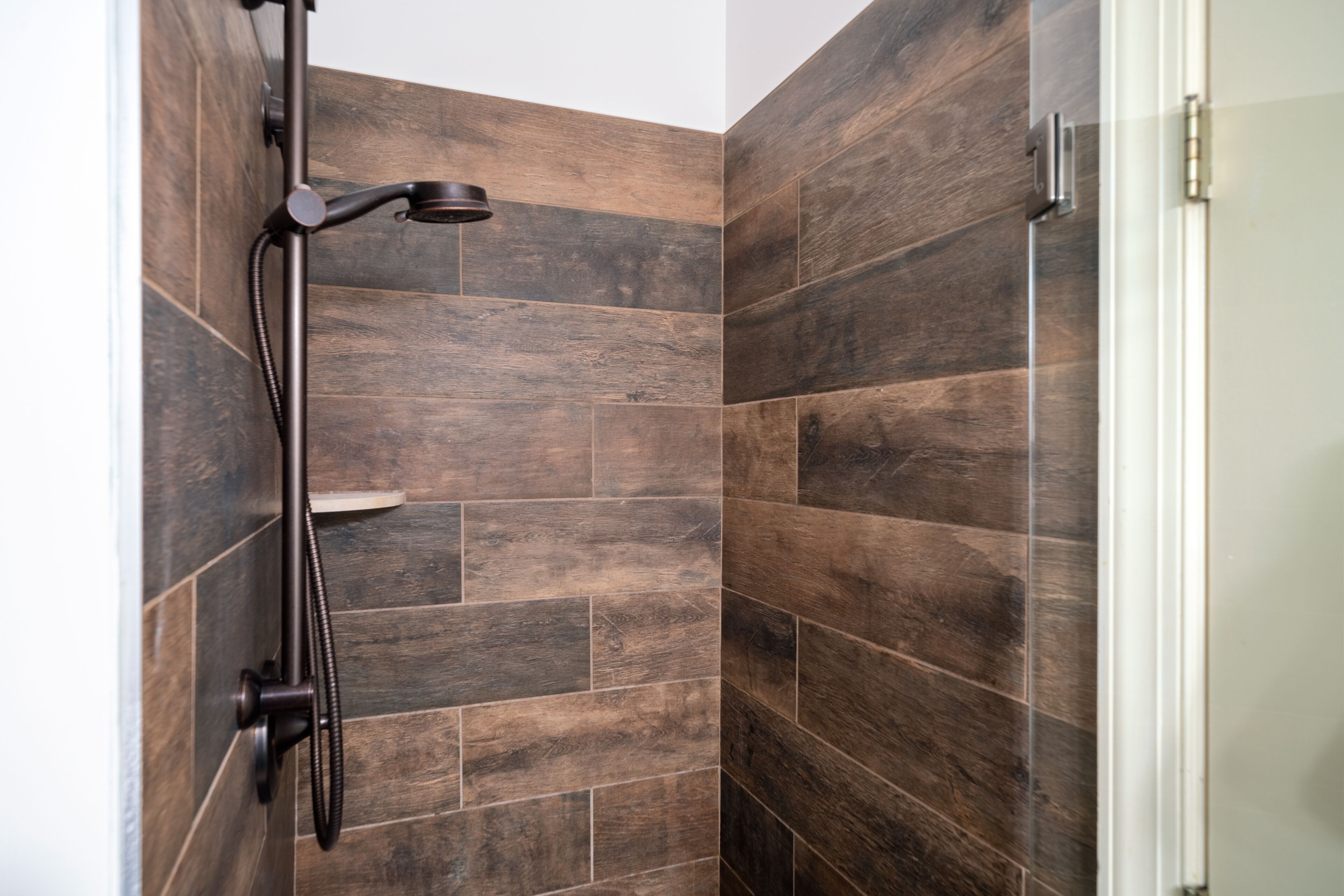 A shower area with dark wooden tiles and a modern showerhead.