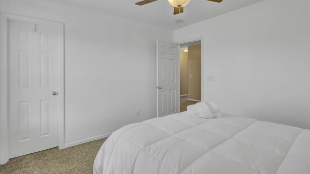 Un dormitorio con una cama blanca, un ventilador de techo y una puerta que da a un armario.