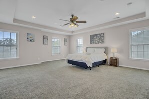 A spacious bedroom with a large bed, ceiling fan, and multiple windows.