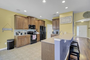 A modern kitchen with wooden cabinets, a central island, and a coffee sign.