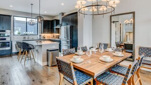 A modern kitchen with stainless steel appliances, a wooden dining table set for six, and a large mirror above the table. - Downtown WP Event Center Loft 96 I Rooftop Spa I Great Views I Bunks I Discounted Attractions (Winter Park)