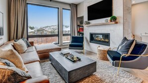 A modern living room with a sofa set, a coffee table, a fireplace, and a large TV mounted on the wall. - Downtown WP Event Center Loft 96 I Rooftop Spa I Great Views I Bunks I Discounted Attractions (Winter Park)