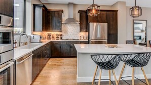 A modern kitchen with dark wood cabinets, stainless steel appliances, and a central island with bar stools. - Downtown WP Event Center Loft 96 I Rooftop Spa I Great Views I Bunks I Discounted Attractions (Winter Park)