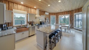 Une cuisine spacieuse avec un lambris en bois, un grand îlot central doté de tabourets de bar et une vue sur l’extérieur grâce à de grandes fenêtres.