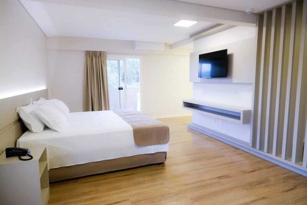 Moderni hotellihuone, jossa on sänky, seinälle asennettu taulutelevisio ja puulattia.