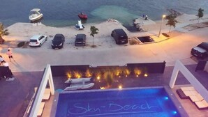 Ein Pool mit der Aufschrift 'Sky Beach', umgeben von Liegestühlen und Blick aufs Meer.