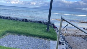 Een verhard pad leidt naar een gazon met een metalen hek, met uitzicht op een strand en de oceaan.