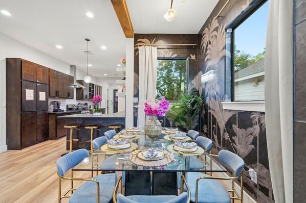 A modern kitchen with dark wood cabinets, a central island, and a dining area with a glass table and blue chairs.