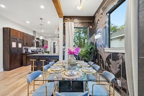 Una cocina moderna con armarios de madera oscura, una isla central y una zona de comedor con mesa de vidrio y sillas azules.