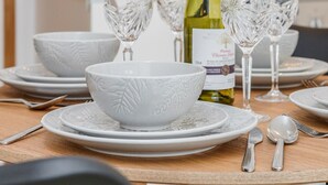 Une table à manger dressée avec de l’assiette, des bols et des couverts blancs, une bouteille de vin et deux verres à vin.