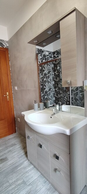 Ein modernes Badezimmer mit einem großen Waschbecken, einem Spiegel und einem Holzkabinet.