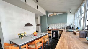 Una cocina moderna con comedor, que cuenta con piso de baldosas de piedra, sillas de madera y lámparas colgantes.