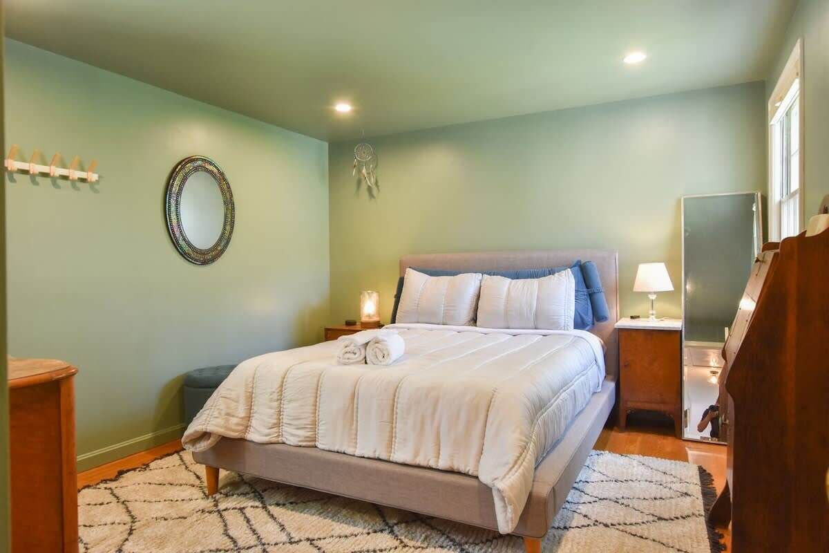 Un dormitorio con cama, mesitas de noche, un espejo y un atrapasueños en la pared.