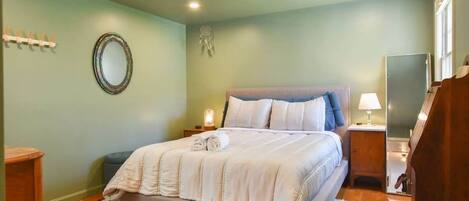 Un dormitorio con cama, mesitas de noche, un espejo y un atrapasueños en la pared.