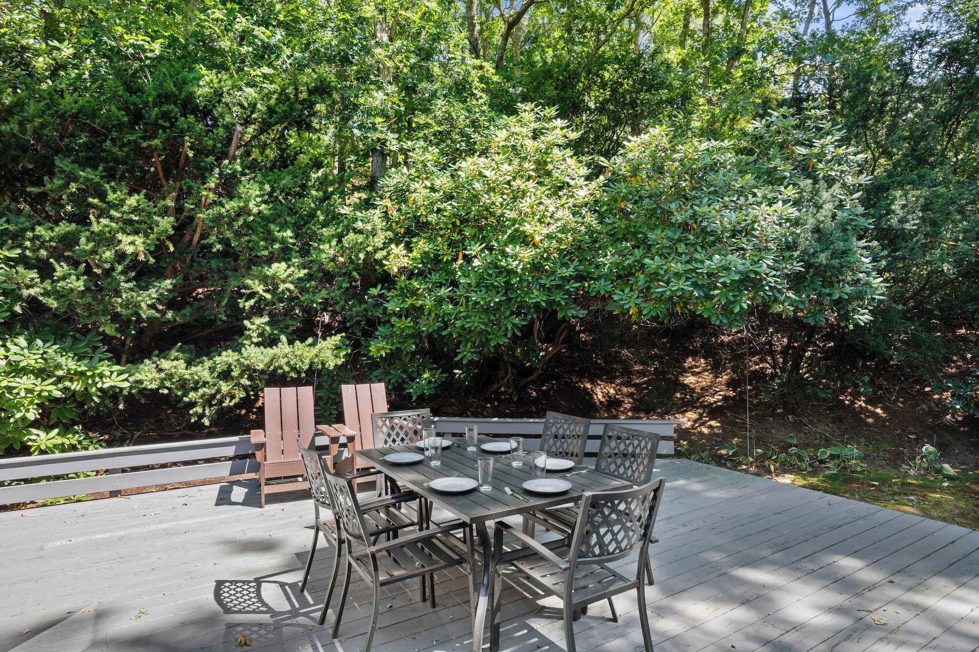 Un área de comedor al aire libre con terraza de madera, sillas de metal y una mesa preparada para cuatro comensales.