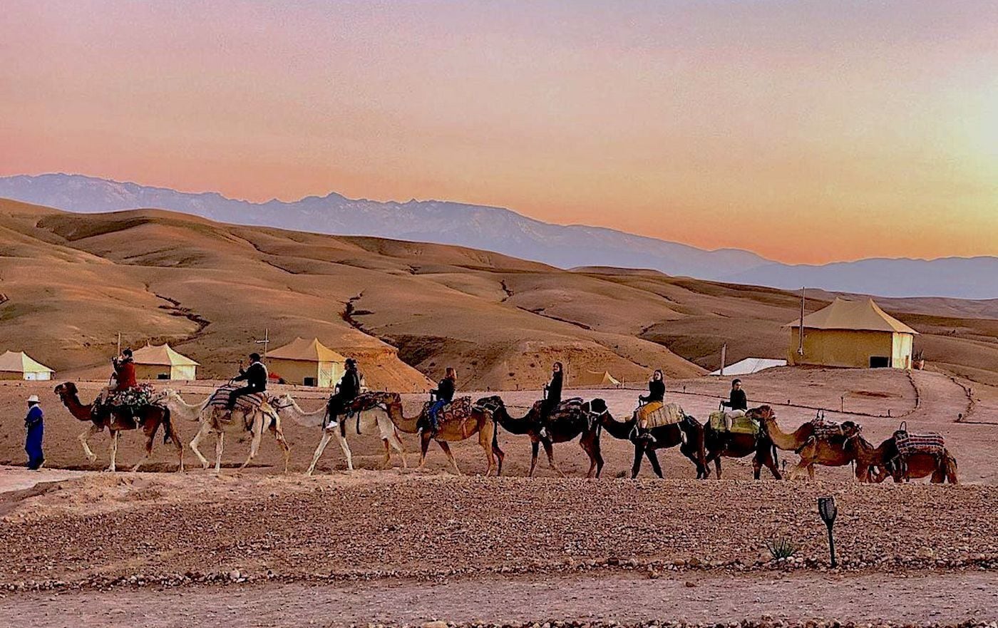Paisaje desértico con tiendas de campaña y camellos.