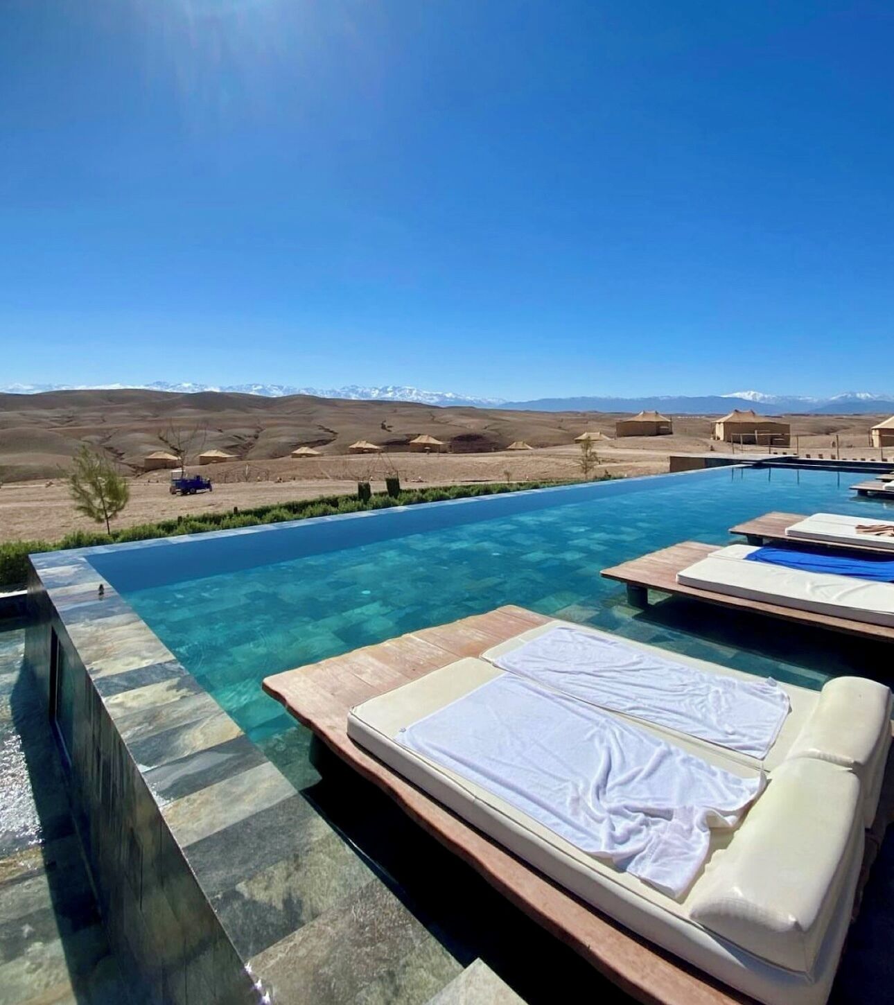 Una piscina azul cristalina con sillas de descanso y vistas a las montañas.