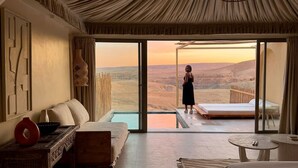 Una habitación con un gran ventanal corredizo que da a una piscina, un sofá, una mesita y vistas a un paisaje desértico.