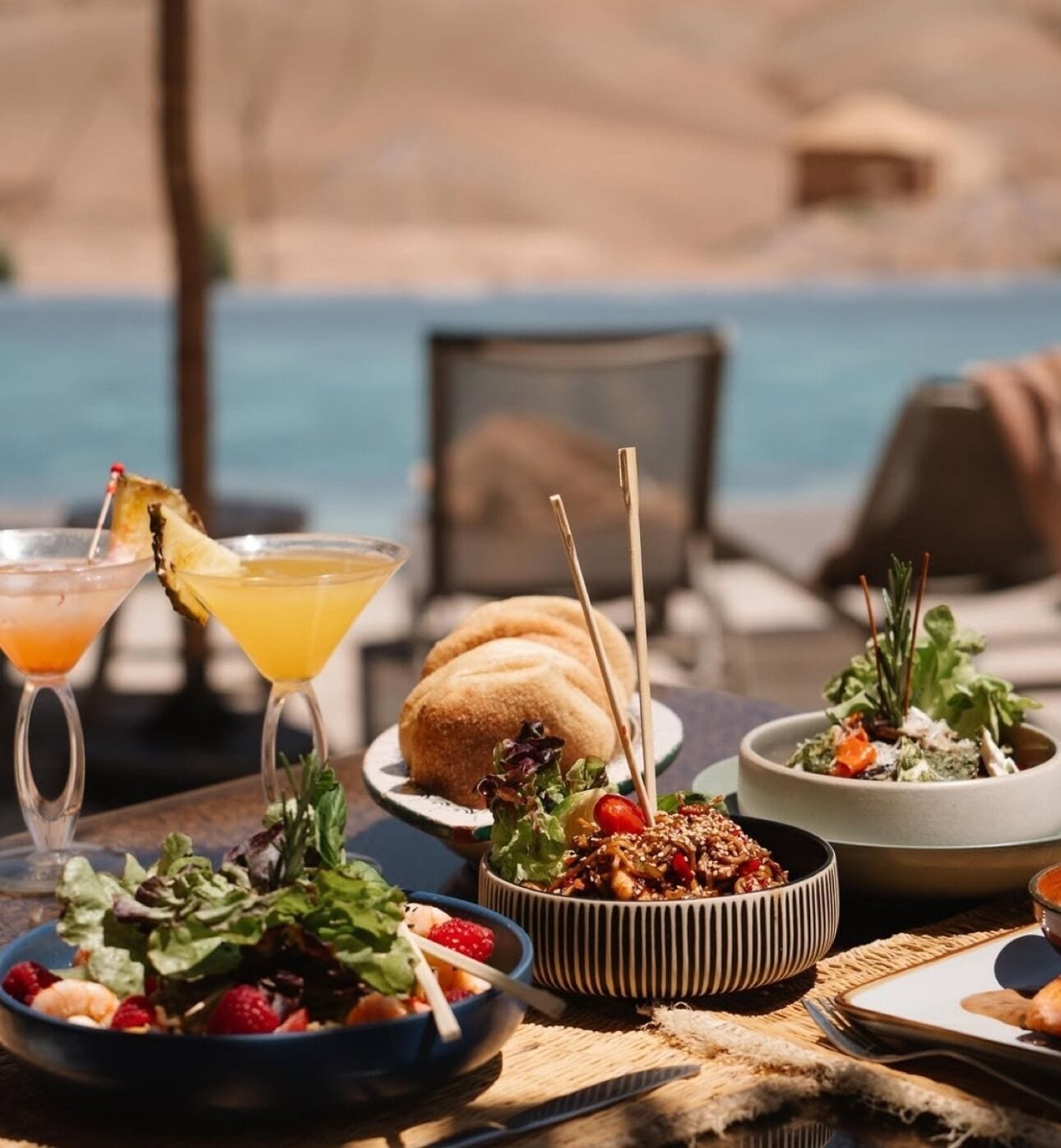 A table with food and drinks, a pool in the background, and outdoor seating.