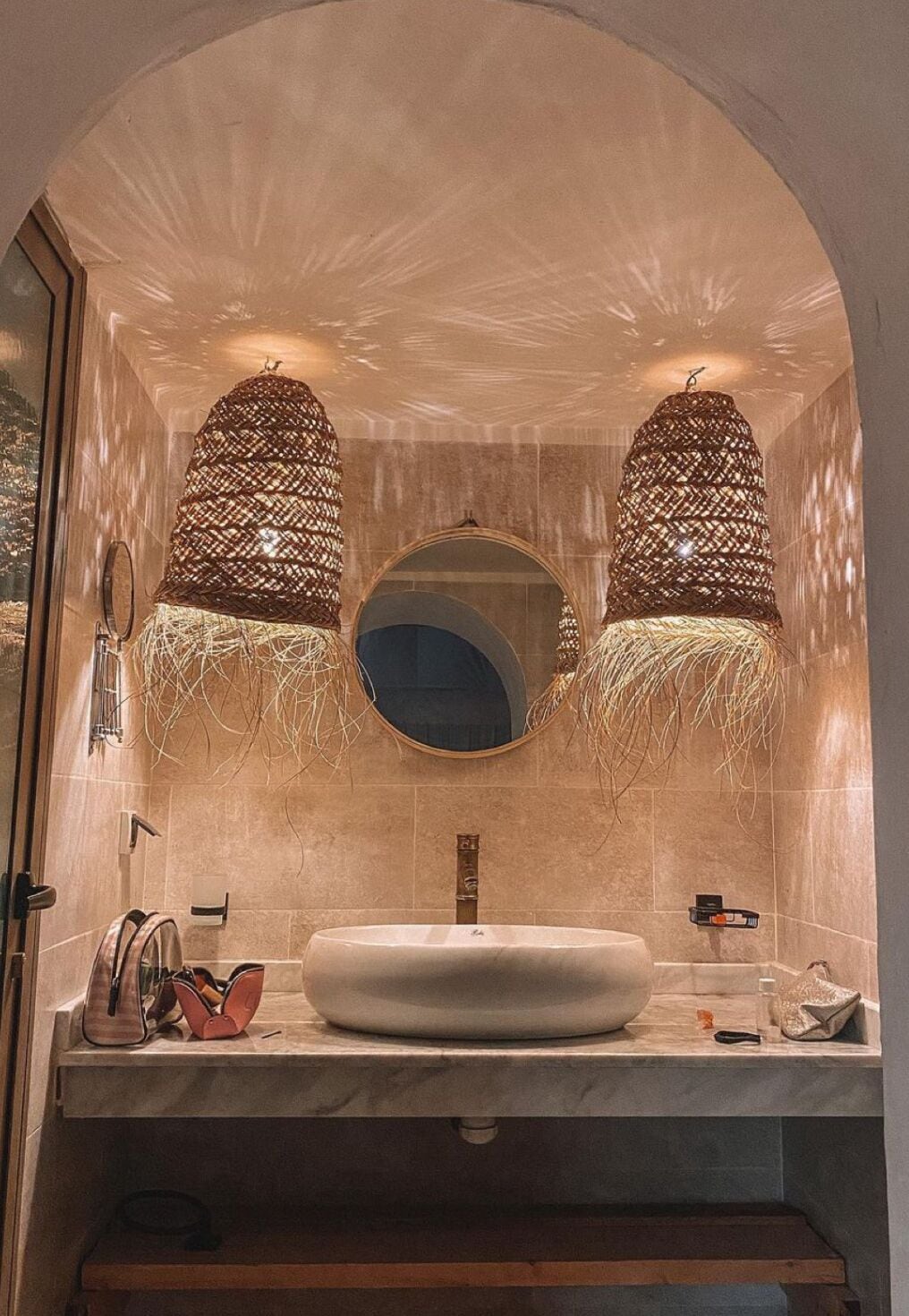 A bathroom with a large arched mirror, a round mirror, and two hanging woven light fixtures.