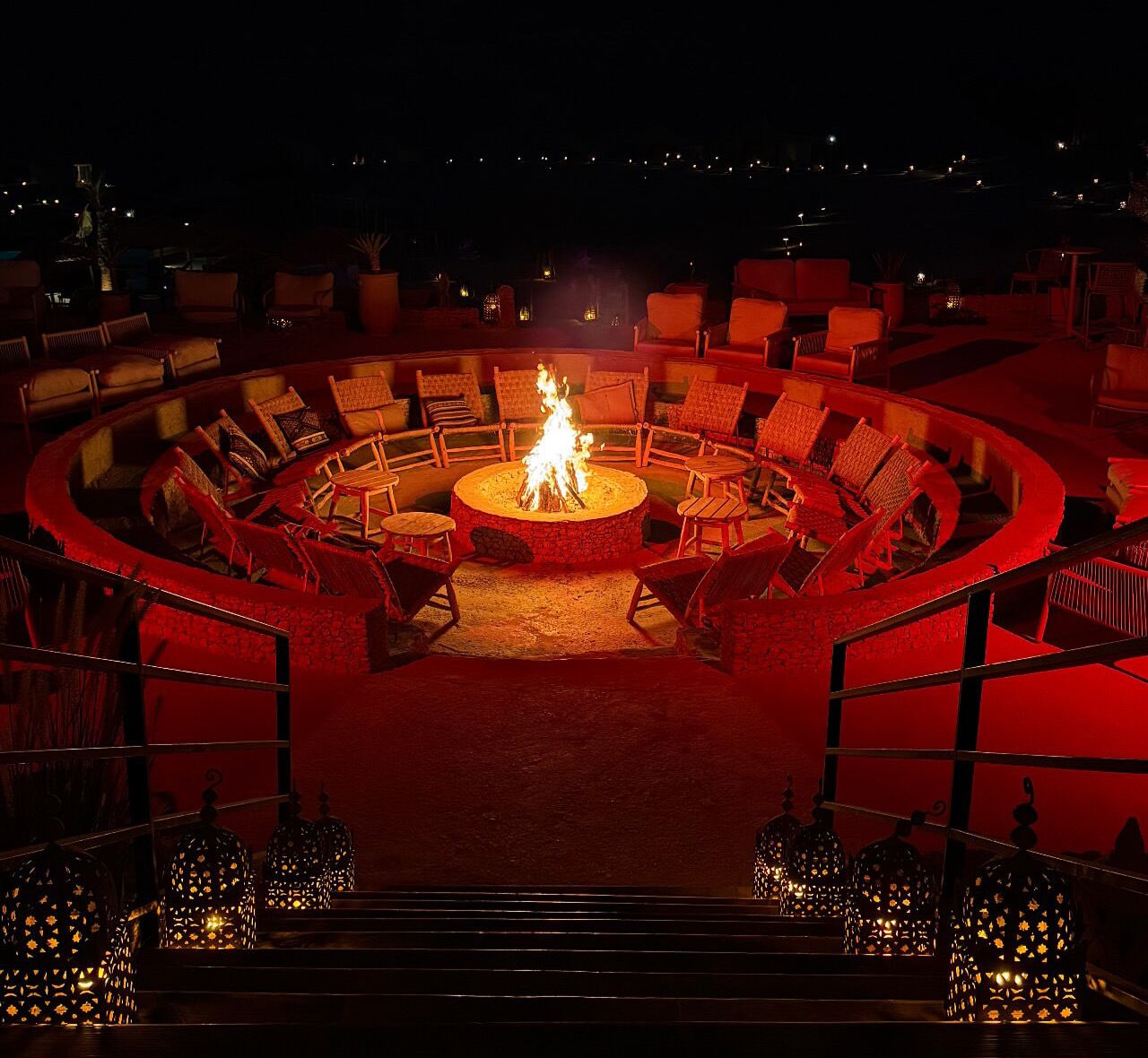 A circular outdoor seating area with a central fire feature, surrounded by chairs and lanterns.