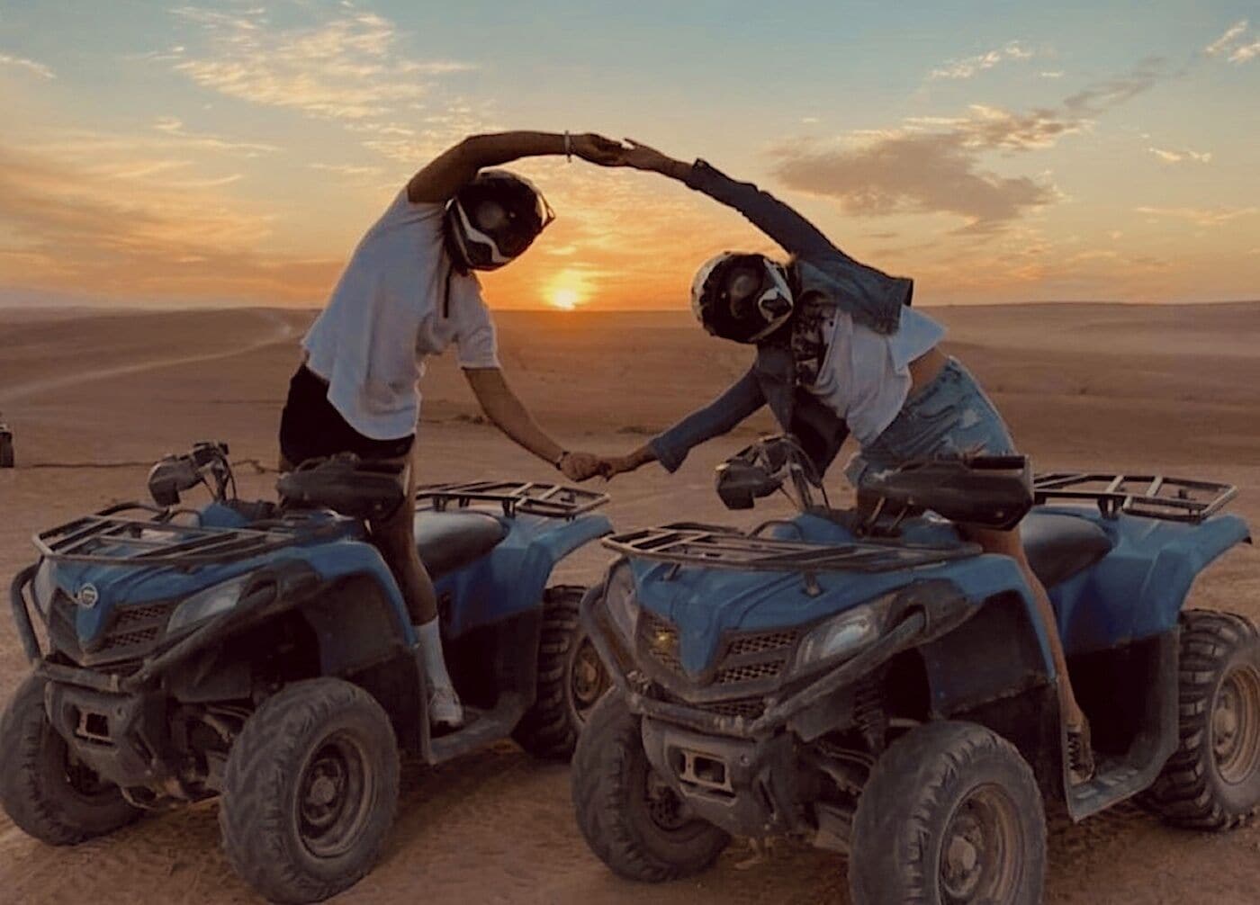 Dos personas conduciendo cuatrimotos en un paisaje desértico con un atardecer.