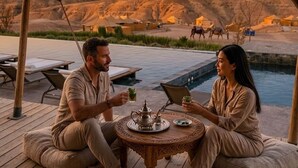 Ein Paar sitzt auf einer Holzterrasse mit Blick auf eine Wüstenlandschaft und einen Pool.