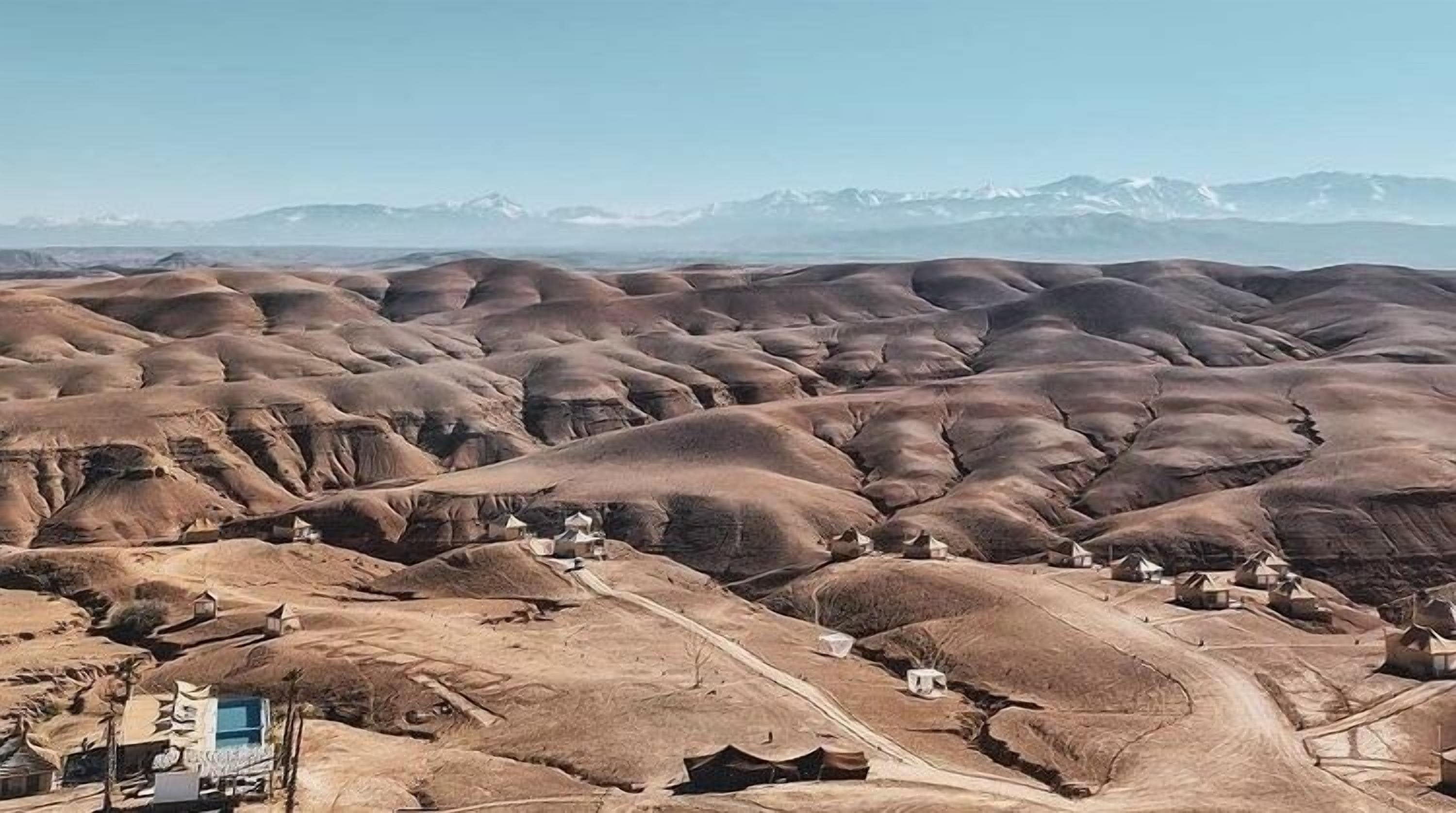Vista panorámica de un paisaje desértico con colinas ondulantes y un pequeño asentamiento con edificios dispersos.